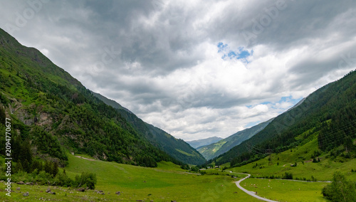 Принти на полотні Panoramic view across a green alpine valley beneath dark clouds