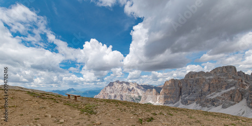 Konstfotografi Wooden bench on alpine plateau overlooking rugged dolomite peaks under dramatic