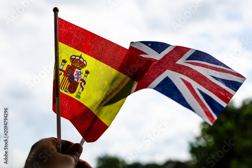 Bright Spain flag takes focus with the Union Jack below held by a hand under clouded light portraying friendly ties education abroad goals and the excitement of international events