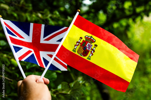 Schilderij op canvas A close view of the British and Spanish flags held aloft in green surroundings c
