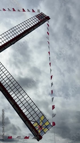 Traditional windmill with colorful festive pennant flags viewed from below during outdoor celebration. Cultural heritage, tourism, festival, architecture, traditional craftsmanship, public event