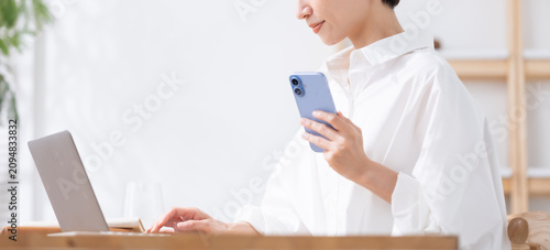 Bild auf Leinwand スマホを持ってパソコンを使う女性
