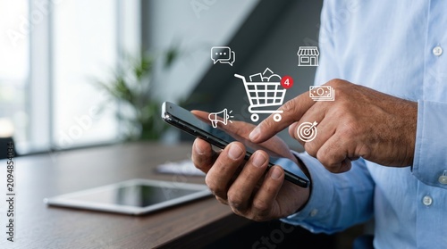 Close-up of man hand using smartphone for online shopping with floating e-commerce icons including cart, store and payment symbols