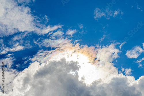 Sunlit iridescent cirrus clouds displaying atmospheric diffraction beneath towering cumulus formation