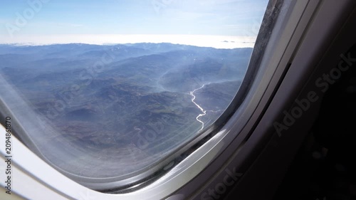 Airplane window view of a shining river and mountains during commercial air travel and tourism