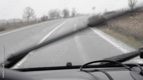 Car driving on a wet, winding road with wipers cleaning the windshield on a foggy and rainy day. Road safety, adverse weather and careful driving.