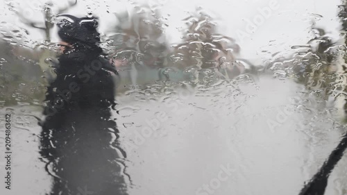 Gloomy rainy day seen through a wet car window conveying melancholy atmosphere with a woman dressed in black under the rain