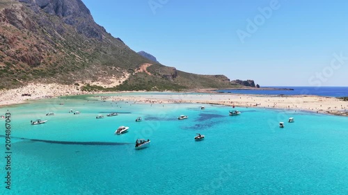 Aerial drone view of Balos Lagoon with crowds on the white-sand beach below rugged mountains, Balos, Greece