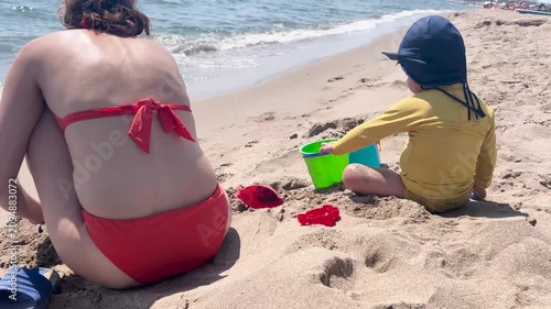 Mother and child playing with sand on a sunny summer beach