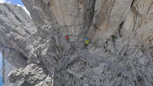 Two hikers crossing an exposed cliffside ledge on Via Ferrata Bocchette Centrali above Brenta Valley, Italy