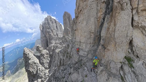 Panoramic view of two hikers traversing Via Ferrata Bocchette Centrali with Campanile Alto in the Brenta Dolomites