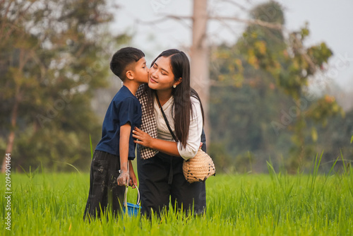 A loving Asian boy kissing his mother on the cheek in a green rice field, happy family enjoying sweet moment together during authentic rural lifestyle outdoor.