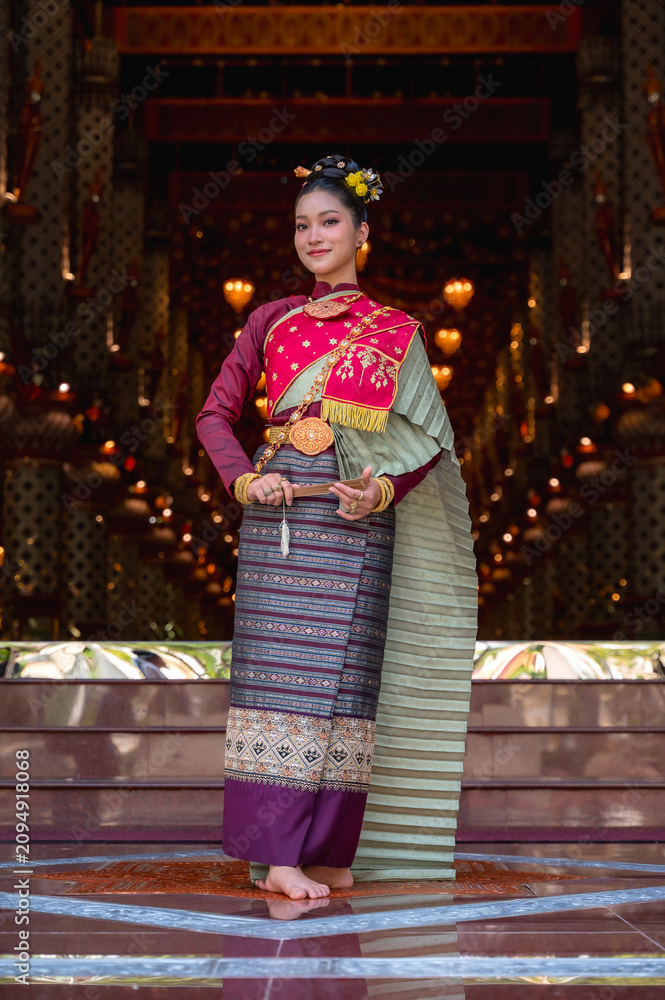 Fototapeta premium Thai woman in elegant traditional Royal Chakraphat dress and golden jewelry holding folding fan, posing inside ancient temple vihara