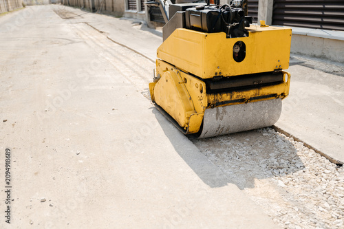 Obraz na plátně Yellow road roller machine compacting ground surface on construction site for pa