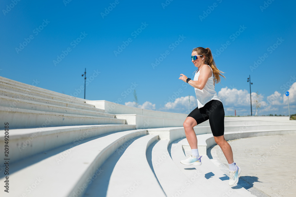 Fototapeta premium Woman exercising on outdoor steps under a bright blue sky on a sunny day while wearing stylish athletic gear