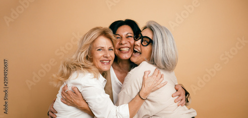 Foto Group of three mature women sharing a joyful hug, smiling while looking at camer