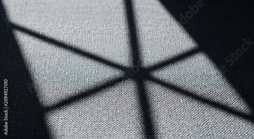 Abstract criss-cross window shadow pattern cast onto a textured white or light grey fabric surface. The diagonal dark lines create a grid effect across the cloth material