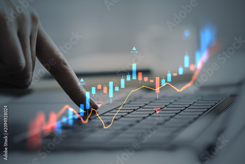 Finger pressing laptop keyboard with glowing candlestick chart and rising gra...