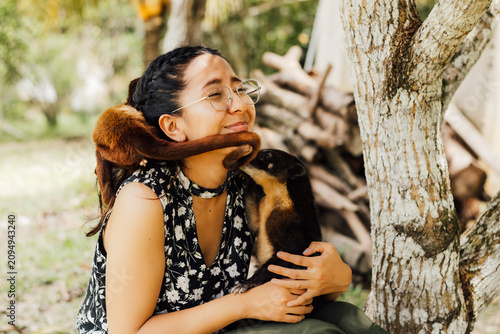 Konstfotografi Mujer feliz al aire libre interactuando con un pequeño mono y un coatí con cariño, celebrando la conexión con la fauna en el Día Mundial de los Animales