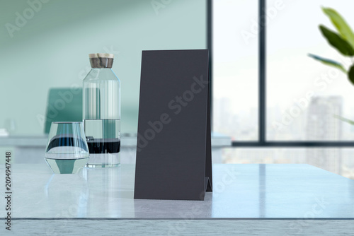 Black table tent mockup standing on marble countertop with water bottle and glass against blurred office window background for menu design. 3D Rendering