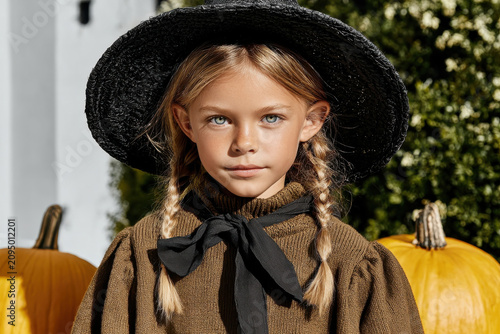 Portrait of girl with braided hair and wide black hat standing near pumpkins outdoors