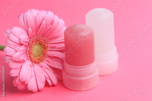 Natural crystal alum deodorant with a pink flower on a pink background