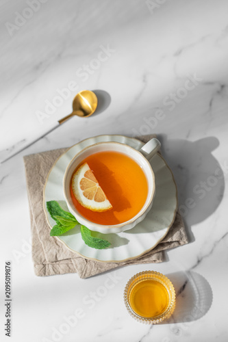 Cup of tea with lemon and mint on a marble background with spoon and honey