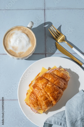 A golden croissant sandwich with ham and cheese on a white plate on a tile background