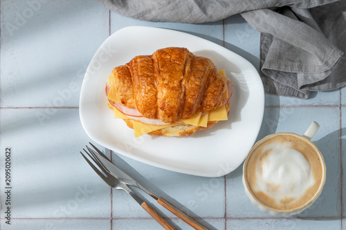 A golden croissant sandwich with ham and cheese on a white plate on a tile background