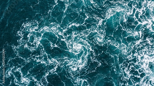 Aerial view of turbulent deep blue ocean water with swirling white foam patterns and currents