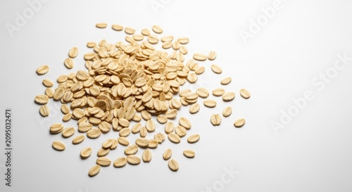 A scattering of dry rolled oats spread across a clean white surface, showcasing natural textures and pale golden tones in bright light, wellness, meal, gluten-free