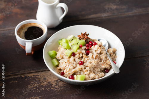 Fotografie Porridge with berries, chopped kiwi and cup of coffee on wooden table background