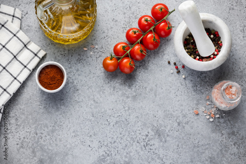 Spices, olive oil and cherry tomatoes on grey stone background. Top view with copy space