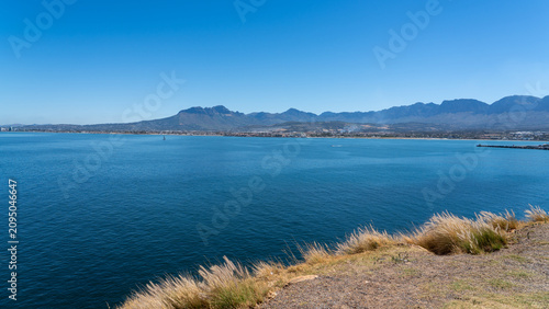 Panoramic viewpoint above Gordon’s Bay overlooking False Bay, Table Mountain and the Cape Peninsula under a deep blue sky. Scenic starting point of South Africa’s Whale Coast Route.