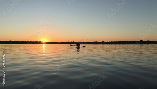 Kayaker Moves on Water as Sun Sets Over the Horizon Near Wooded Area