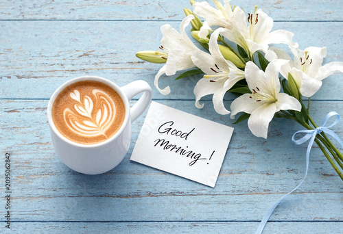 Beautiful white lilies with a hot latte and good morning card on rustic table