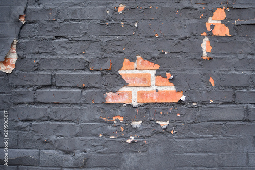Gray wall with paint peeling to reveal red bricks