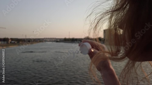 Contemplative Waterside Portrait: Young Woman Blow Soap Bubbles Gazing Across Riverine Landscape at Golden Hour