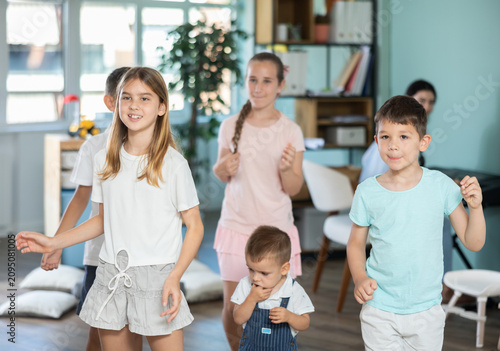 Children actively jump and dance during music lesson, teacher accompanies on piano in kindergarten, music lesson...