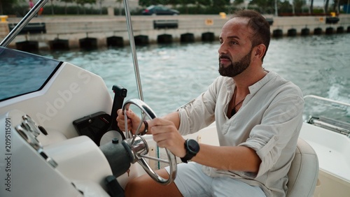 Billede på lærred Bearded man steering a boat in a marina on a summer getaway