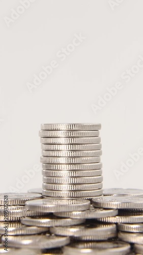 A tall neat stack of silver coins stands in the center of a pile of coins on a light gray background in a seamless loop, highlighting the concept of growth, savings and wealth. Looping video