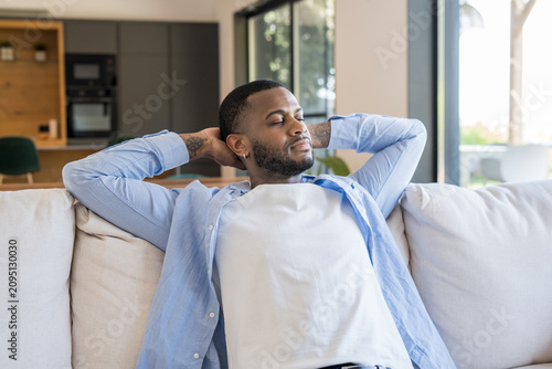 Fotografie Young man unwinding on a comfortable couch at home, eyes closed and hands behind