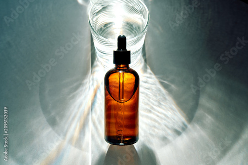 Amber dropper bottle and glass water with light reflections