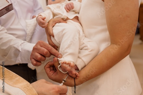 Photos Priest anointing baby foot during baptism ceremony in church with white clothing and warm lighting