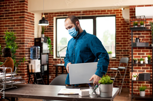 Εκτύπωση καμβά Bearded manager wearing a protective mask carries a laptop into a modern startup office, ready for a busy workday and business planning