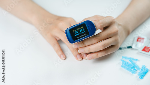 Fotografie Close-up of an adult checking blood oxygen saturation and pulse rate with a fingertip pulse oximeter at home