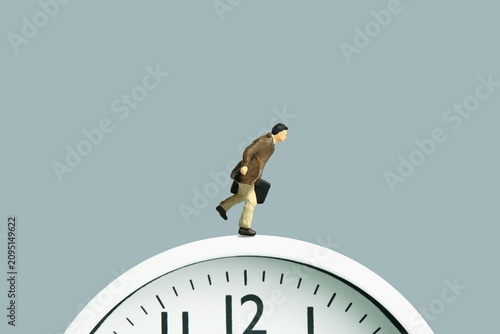 Miniature tiny people toy figure photography. A businessman running above clock carrying briefcase. Isolated on grey background