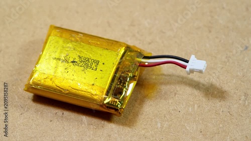 Swollen lithium-ion pouch battery with three-wire connector and thermistor on workbench, close-up panning video of a damaged rechargeable cell representing fire hazard, e-waste and unsafe electronics
