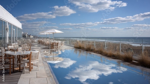 Outdoor dining area overlooks oceanfront beach with calm water reflecting bright blue sky