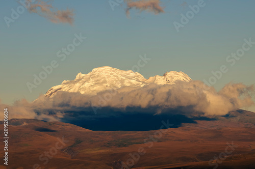 Snow-capped Antisana Volcano amidst Orographic Clouds at Sunset in Ecuador